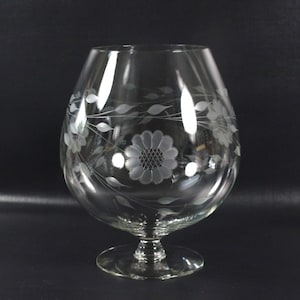 Peut inclure: Un verre à cognac en verre transparent avec un délicat motif floral gravé. Le motif gravé présente une fleur centrale entourée de feuilles et de vignes.