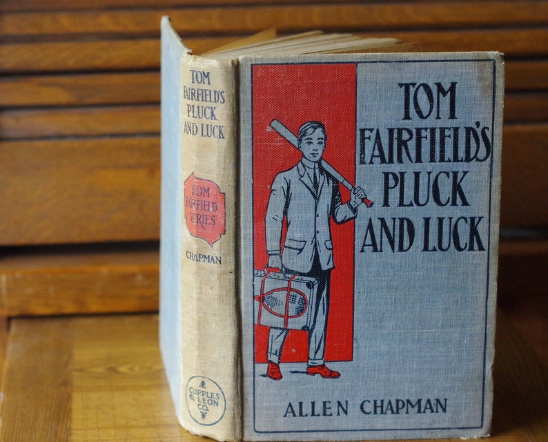 May include: A vintage book titled "Tom Fairfield's Pluck and Luck" by Allen Chapman. The cover features a boy in a suit holding a baseball bat and a suitcase. The book is part of the "Tom Fairfield Series" and published by Cupples & Leon Co.