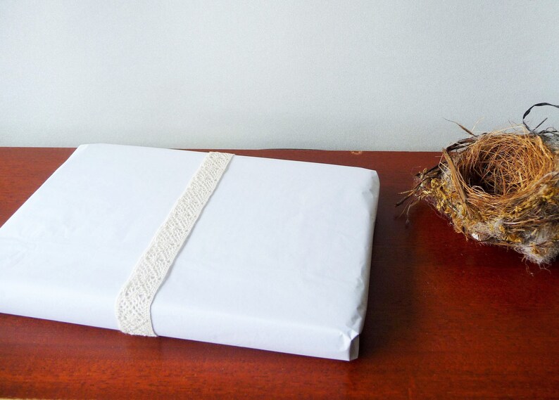 May include: A white gift box wrapped with a white lace ribbon. The box is sitting on a wooden surface.