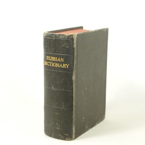 Op de afbeelding: Een zwart, versleten, in leer gebonden boek met gouden letters die "RUSSIAN DICTIONARY" lezen.