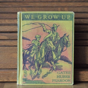 Puede incluir: Una portada de libro infantil vintage con un esquema de color verde y amarillo. La portada presenta una ilustración de dos niños montando a caballo. El título del libro es "We Grow Up" y el autor es Gates Huber Peardon.