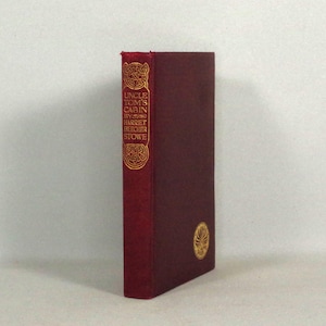 May include: A burgundy hardback book with gold lettering on the spine. The title is "Uncle Tom's Cabin" by Harriet Beecher Stowe.