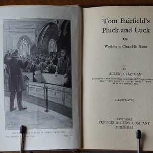 May include: A black and white illustration of a book cover for "Tom Fairfield's Pluck and Luck, or Working to Clear His Name" by Allen Chapman. The book cover features a scene of people in a church.