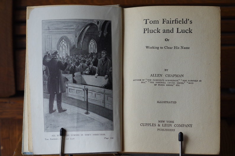 May include: A black and white illustration of a book cover for "Tom Fairfield's Pluck and Luck, or Working to Clear His Name" by Allen Chapman. The book cover features a scene of people in a church.