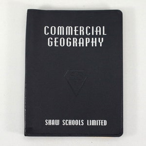 May include: A dark blue book with the title "COMMERCIAL GEOGRAPHY" in white lettering. The book has a white diamond-shaped logo with the letters "SS" inside. The bottom of the book reads "SHAW SCHOOLS LIMITED" in white lettering.