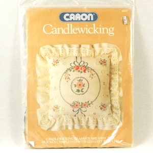 May include: A vintage Caron Candlewicking kit featuring a cream-coloured pillow with a floral embroidery design. The kit includes instructions and materials for creating a decorative pillow.