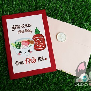 May include: Greeting card with a red border and a white interior. The card features a cartoon bowl of pho and a hot sauce bottle. Text reads "You are the only one Pho me." A pink envelope is included.