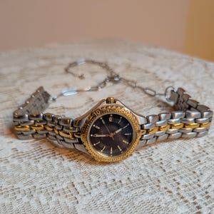 May include: A two-tone wristwatch with a silver and gold band and a dark blue face. The watch has a gold bezel with numbers and markers. The watch is a Pulsar brand.