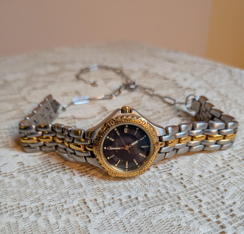 May include: A two-tone wristwatch with a silver and gold band and a dark blue face. The watch has a gold bezel with numbers and markers. The watch is a Pulsar brand.