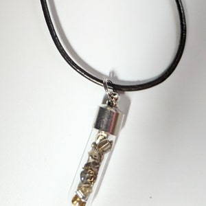 May include: A silver necklace with a black leather cord and a glass vial pendant filled with small metal and glass beads.