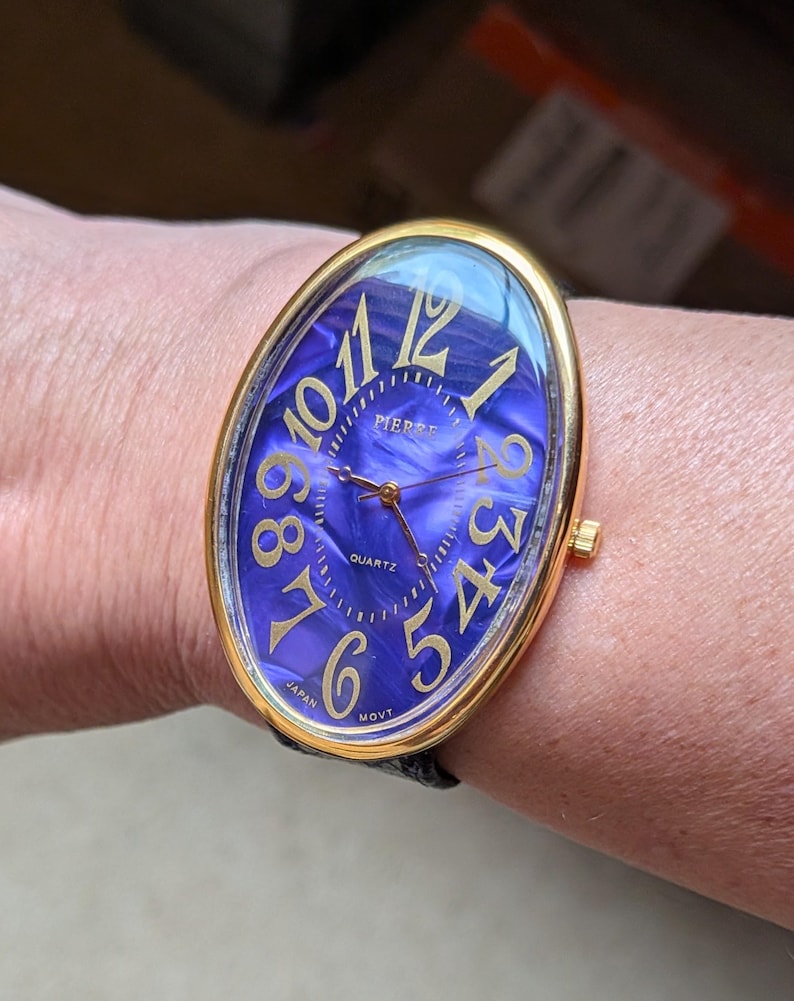 May include: A gold-toned oval wristwatch with a blue marbled face and gold numerals. The watch face reads "PIERRE QUARTZ" and has a black leather band. The watch is marked "JAPAN MOVT".