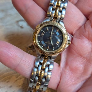 May include: A silver and gold-toned Pulsar watch with a black dial. The watch features a date display and a stainless steel band with gold accents. The watch is water resistant to 100 meters.