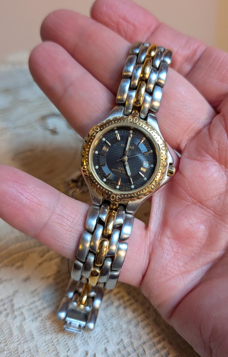 May include: A silver and gold-toned Pulsar watch with a black dial. The watch features a date display and a stainless steel band with gold accents. The watch is water resistant to 100 meters.