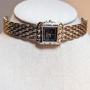 May include: A silver Fossil watch with a black face and silver hands. The watch has a square face and a silver metal band.