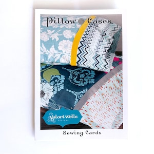 May include: A card featuring various pillowcase designs. The pillowcases showcase floral, chevron, and abstract patterns in shades of blue, green, and pink. The card also displays the text "Pillow Cases" and "Sewing Cards."