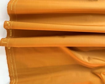 May include: A close-up of a folded piece of fabric in a rich, mustard yellow color. The fabric has a smooth, slightly shiny surface and is likely a cotton blend.