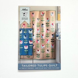 May include: A sewing pattern package featuring a quilt design with tulip motifs. The package includes a blue and a beige quilt with tulip patterns. The text "TAILORED TULIPS QUILT" is visible, along with "10" PRECUT FRIENDLY - BABY & LAP QUILT SIZES INCLUDED."