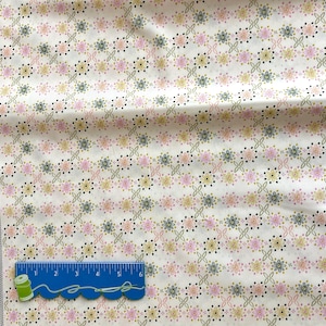 May include: White fabric with a repeating pattern of small pink, yellow, and green flowers. The fabric is folded in half and a ruler is placed on top of the fabric.