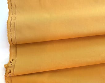 May include: Close-up of folded golden-yellow fabric. The fabric has a smooth texture and a slight sheen. The edge of the fabric shows a printed ruler and the words "SEE THE DIFFERENCE" and "100% PREMIUM".