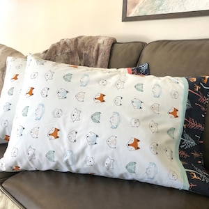 May include: Two white pillowcases with a repeating pattern of animal faces, including foxes, hedgehogs, and bears. The pillowcases have a blue and white trim and a dark blue and white patterned border.