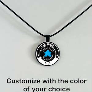 May include: A black pendant necklace with a round, black pendant. The pendant features the text "I AM ALWAYS BLUE" in white, with a blue figure in the center. The necklace has a black cord. The text "Customize with the color of your choice" is below the pendant.