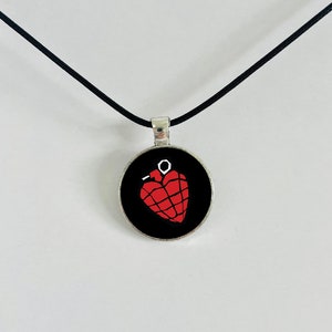 May include: A black necklace with a silver pendant featuring a red heart-shaped grenade graphic.