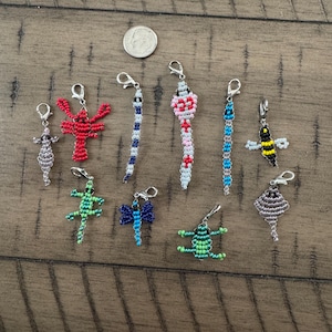 May include: A collection of ten animal-shaped beaded charms with silver-tone lobster clasps, including a lobster, snake, bee, lizard, dragonfly, frog, and stingray. A US dime is included for scale, measuring approximately 0.7 inches in diameter.