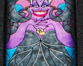 Op de afbeelding: Een hanger in de stijl van een glas-in-loodraam met Ursula, de zeemeermin uit Disney's The Little Mermaid. Ursula is afgebeeld met haar kenmerkende paarse huid, lang wit haar en een ondeugende grijns. Ze draagt een zwarte jurk met een schelpketting en haar tentakels zijn zichtbaar op de achtergrond.