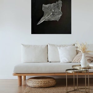 May include: Abstract art piece with a textured, flowing design in shades of silver and white against a black background. The artwork is mounted on a wall above a light-colored sofa, enhancing the room's modern aesthetic.