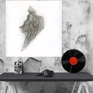 May include: A grayscale watercolor painting of a draped fabric is displayed on a white canvas. A black vinyl record with a red label sits on a black table, along with headphones and a small speaker. The background is a textured, distressed wall.