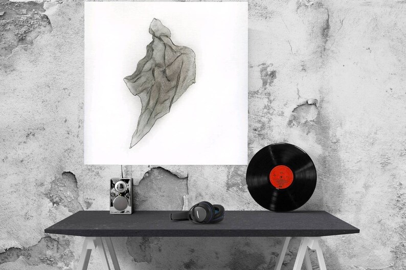 May include: A grayscale watercolor painting of a draped fabric is displayed on a white canvas. A black vinyl record with a red label sits on a black table, along with headphones and a small speaker. The background is a textured, distressed wall.