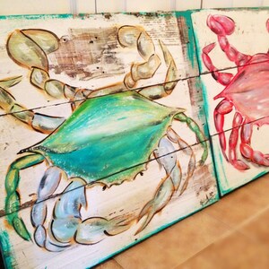 May include: Two painted wooden signs featuring crabs. The sign on the left features a blue and green crab, while the sign on the right features a pink crab.