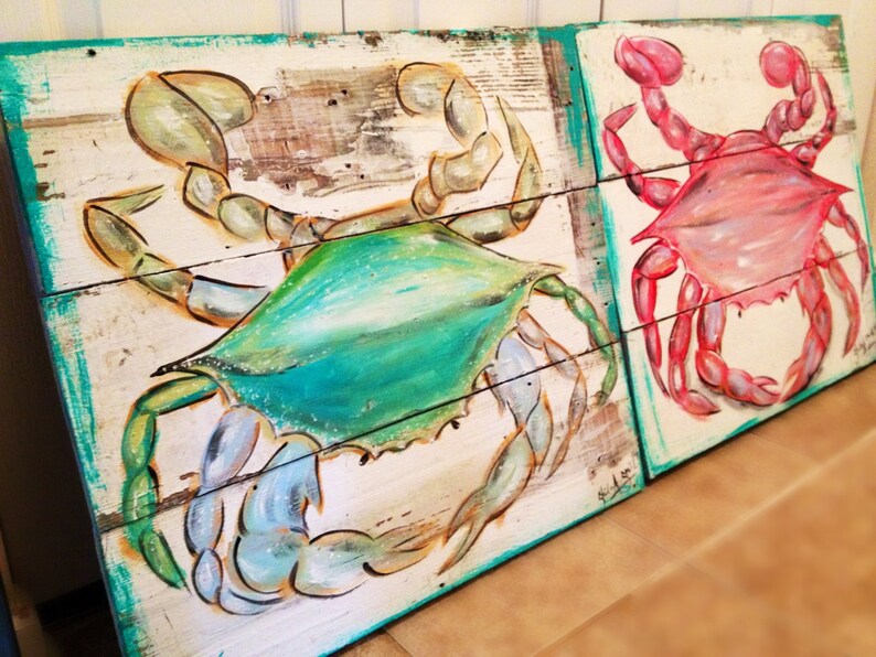 May include: Two painted wooden signs featuring crabs. The sign on the left features a blue and green crab, while the sign on the right features a pink crab.