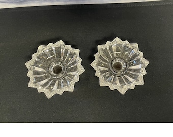 May include: Two clear glass candle holders with a starburst design. The holders have a small, round opening in the center for a candle.