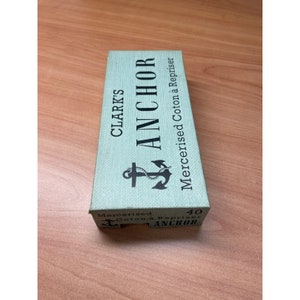 May include: A green box with the text "CLARK'S ANCHOR Mercerised Coton à Repriser 40 ANCHOR" printed on it. The box features a black anchor graphic.