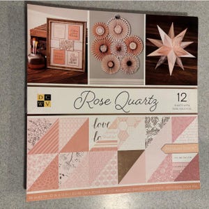 May include: A pack of 12 double-sided printed cardstock sheets in rose quartz and rose gold foil. The pack includes 36 sheets, each measuring 12 inches by 12 inches. The paper features a variety of patterns, including geometric designs, floral motifs, and the words "love" and "lo".