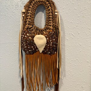 May include: A woven brown leather and feather wall hanging with a fringe of brown leather. The hanging has a white leather heart shape in the center.