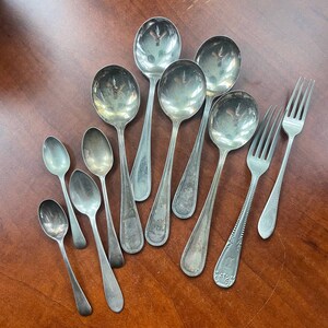 May include: A collection of nine silver spoons and two silver forks. The spoons are of varying sizes and shapes, with some having ornate handles. The forks are both standard size and have a simple design.