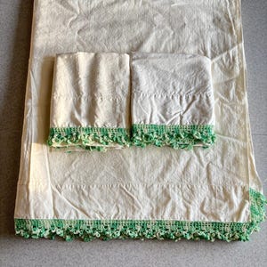 May include: A set of three white pillowcases with green crocheted trim. The pillowcases are made of a soft, lightweight fabric and are perfect for adding a touch of elegance to any bedroom.