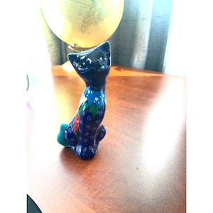 May include: A blue ceramic cat figurine with colorful floral and geometric patterns. The cat is sitting upright with its tail curled around its legs.