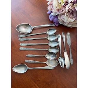 May include: A set of ten silver-plated spoons and two butter knives. The spoons have ornate handles and the knives have simple handles.
