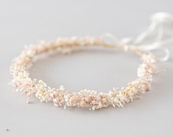 May include: A delicate floral crown featuring small, dried flowers in shades of cream and pale pink. The circular crown is tied with white satin ribbons. Perfect for weddings, festivals, or special occasions.