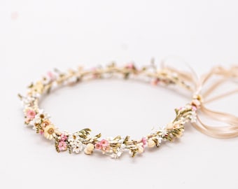 Könnte beinhalten: Eine zarte Blumenkrone mit weißen und rosa Blüten und grünen Blättern. Die Krone ist mit einem beigefarbenen Band gebunden.