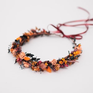 Könnte beinhalten: Eine Blumenkrone aus getrockneten Blumen in Orange-, Rosa- und Rottönen. Die Krone ist auf einer Drahtbasis gefertigt und hat ein burgunderfarbenes Band.