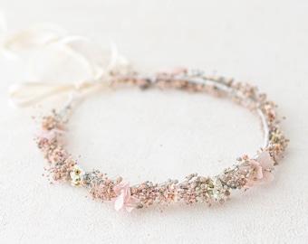 May include: A delicate floral crown made with dried flowers in shades of pink and white. The crown is made with a wire base and is tied with a white ribbon.