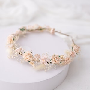 Op de afbeelding: Een delicate bloemenkrans met roze en witte gedroogde bloemen, perfect voor een bruiloft of speciale gelegenheid.