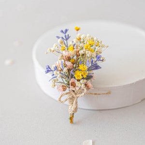 Op de afbeelding: Een klein boeket gedroogde bloemen gebonden met touw. Het boeket bevat gele, roze en paarse bloemen.