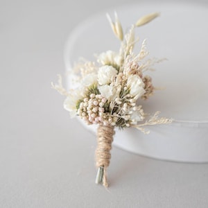 Könnte beinhalten: Ein kleiner Strauß getrockneter weißer Blumen und Grün, gebunden mit Schnur. Der Strauß ist kreisförmig angeordnet und hat einen rustikalen, natürlichen Look.