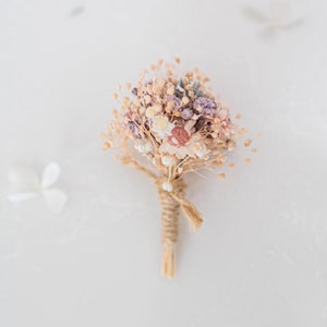 Boutonniere for the groom with dried flowers in pastel colors. Buttonhole with preserved flowers for groomsman with baby&#39;s breath