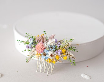 May include: A silver hair comb adorned with a cluster of dried flowers in shades of blue, yellow, pink, and white. The flowers are arranged in a loose, natural style.